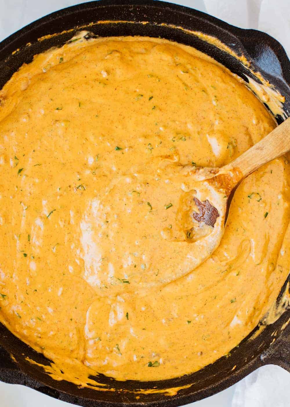 Velveeta chili cheese dip in a cast iron skillet with wooden spoon.