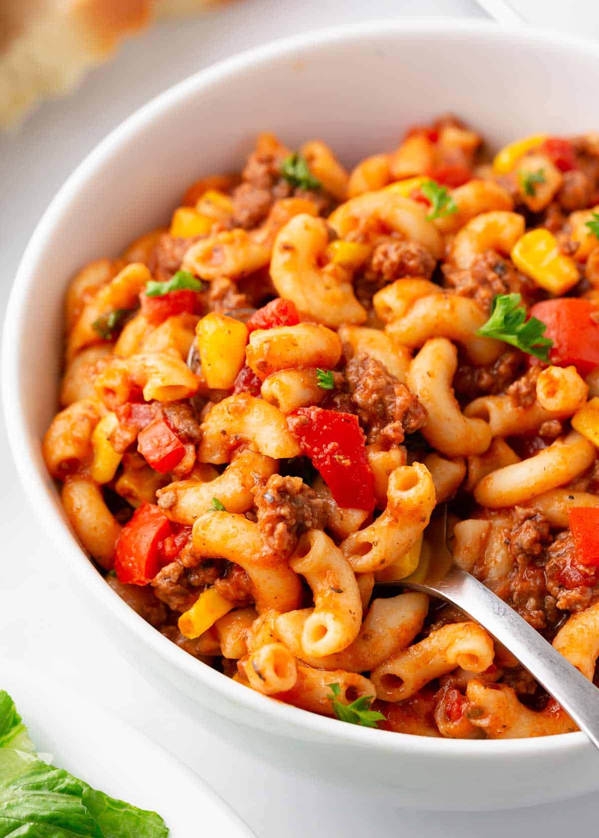 This easy goulash recipe is family-friendly comfort food at it's best! It's a one pot American classic made with beef and pasta simmered in a flavorful tomato sauce. Goulash in a white bowl with a spoon.
