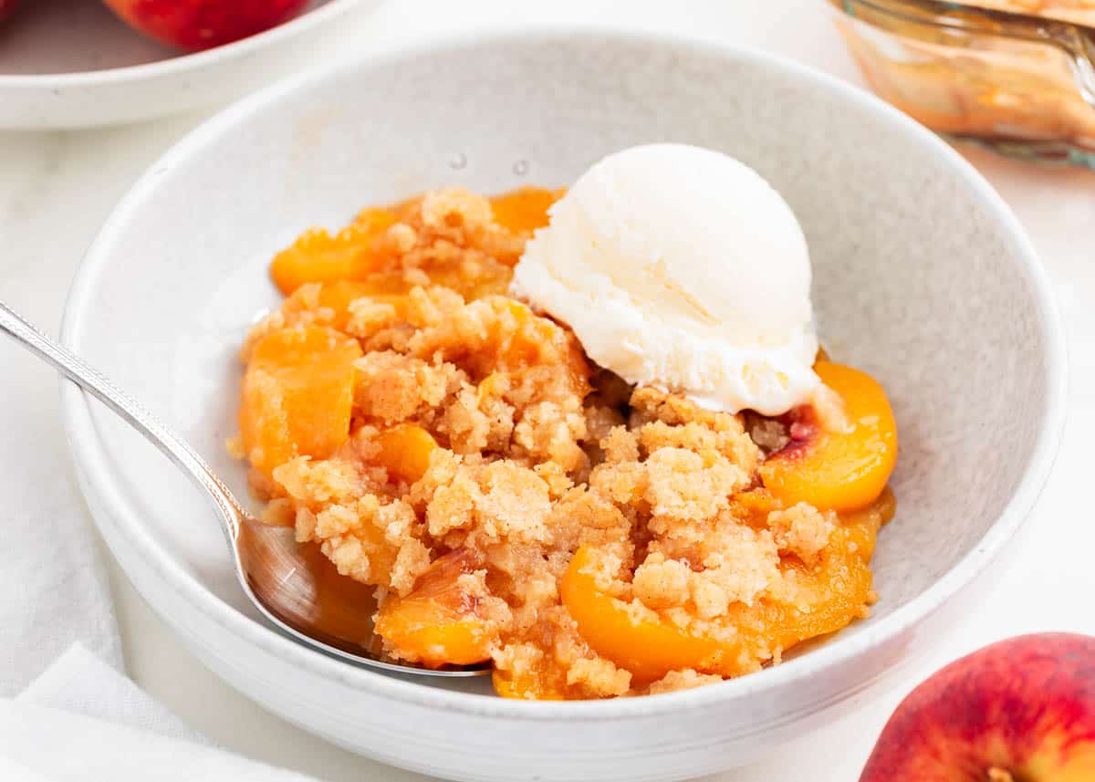 The warm homemade peach filling paired with the buttery sugary topping in this easy peach cobbler recipe is seriously to die for. It's the best summer dessert served warm with vanilla ice cream on top or make it year round with fresh, frozen or canned peaches! Peach cobbler and ice cream in a bowl.