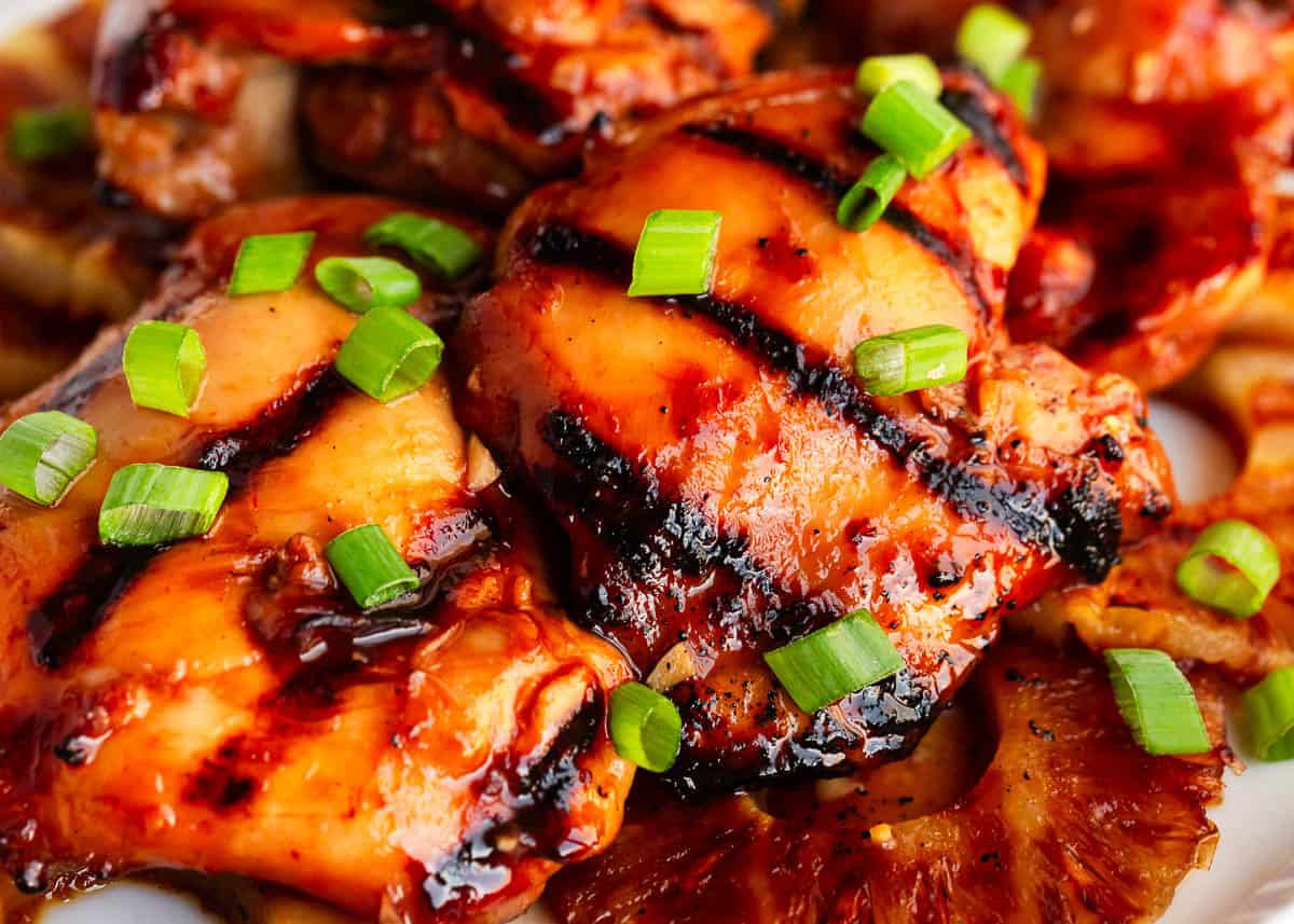 Huli Huli chicken is a Hawaiian favorite with juicy chicken thighs and a sweet, tangy pineapple-soy glaze. Grilled until caramelized and smoky, it's BBQ with a tropical twist! Close up of grilled Hawaiian huli huli chicken with garnish.