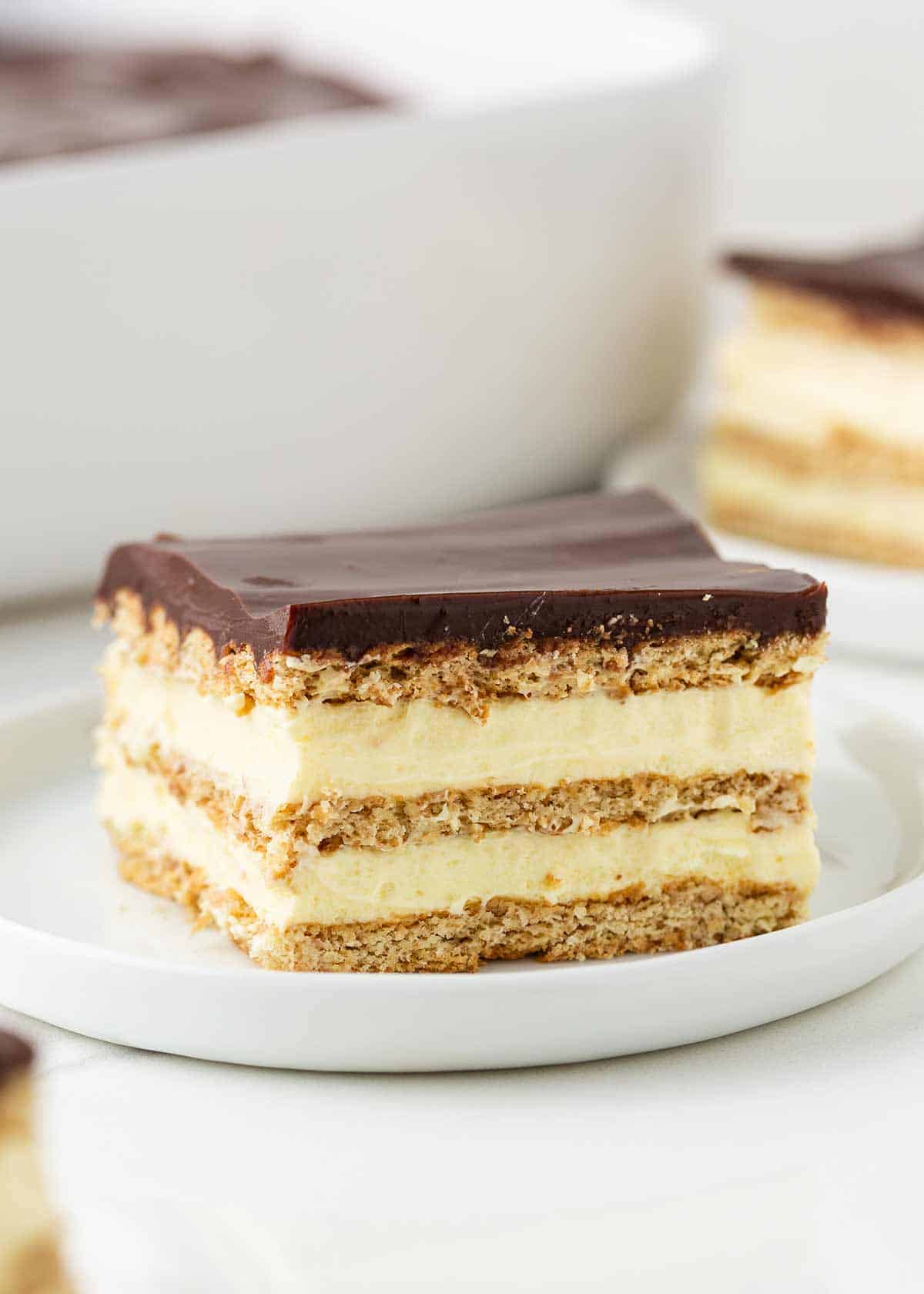 This chocolate eclair cake is an easy no-bake dessert made with layers of graham crackers separated by thick luscious cream and topped with a chocolate frosting. Eclair cake on a plate.